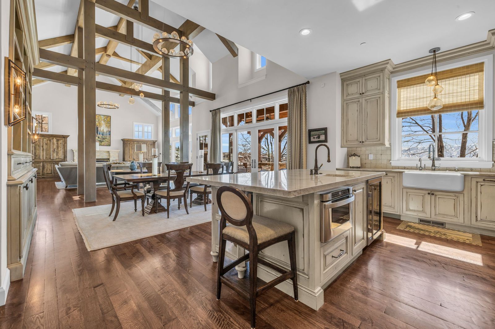 Open-plan kitchen with timber beams, a stone island and a dining table by the windows