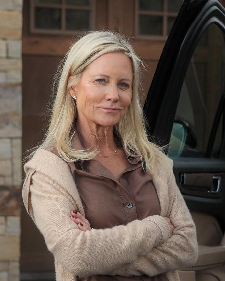 Natalie Siegel standing with her arms crossed beside an open car door in front of a stone and timber home